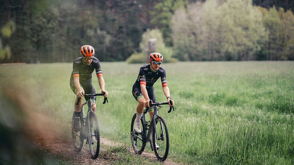 Two riders from Team Heizomat p/b Kloster Kitchen cycle along a forest path