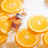 Fruit Shot 1SHOT in un flacone da 30 ml cade in acqua con arance e carote, si possono ancora vedere gli schizzi d'acqua dovuti alla caduta.