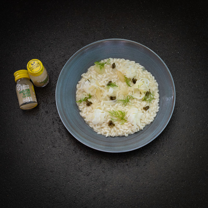 Fennel risotto arranged in a plate. Next to it are two Ginger Shot Classic.