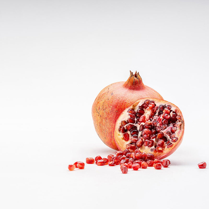 One ingredient of the Pomegranate flavored Ginger Shot: a sliced half pomegranate and a whole pomegranate behind it.