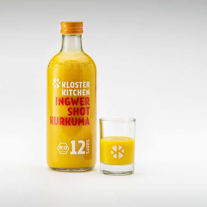 Der Ingwer Shot in der Geschmacksrichtung Kurkuma in der 360 ml Flasche mit einem gefüllten Shot Glas daneben