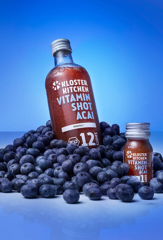 Vitamin Shot Acai 360 ml bottle next to a Vitamin Shot Acai 30 ml bottle. Both bottles are placed in a pile of acai berries.