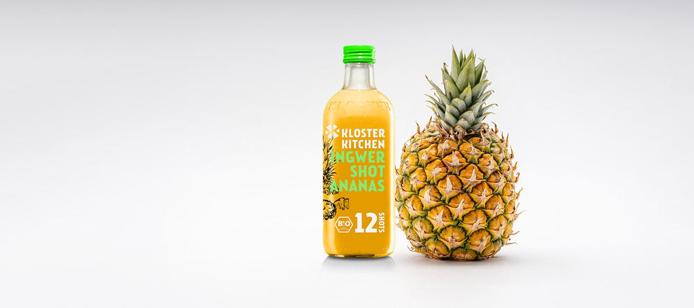 Un shot de gingembre ananas 12SHOTS (bouteille de 360 ml contenant 12 portions) à côté d'un ananas