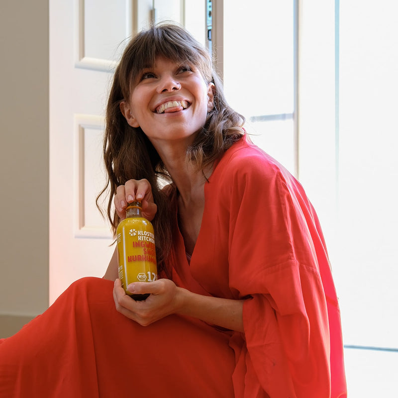 Contenu du kit de dégustation M de shot de gingembre : bouteille de 360 ml de shot de gingembre au curcuma, tenue par une femme souriante en robe rouge. 