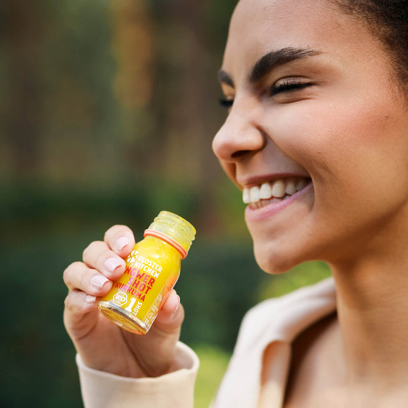 Contents of the Ginger Shot tasting set L: Woman just brings to her lips a Ginger Shot Turmeric in a 30 ml bottle.