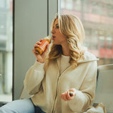 Blonde woman brings the Kloster Kitchen smoothie apple carrot rhubarb to her lips to drink from it.