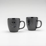 2 tazze Kloster Kitchen. Le tazze sono di colore nero opaco e presentano il logo Kloster Kitchen in nero lucido sulla parte anteriore.