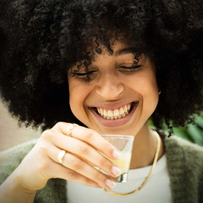 À propos de nous : C'est ce qui nous motive : Nos clients ! Comme par exemple sur cette photo : une femme souriante qui porte un verre à shot à sa bouche.