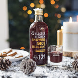 (Flasche im Weihnachtsambiente): Kloster Kitchen Ingwer Shot Beere-Zimt Winter Edition Flasche mit Schnapsglas, im Hintergrund Weihnachtsbaum mit Lichtern, Kerze und Tannenzapfen