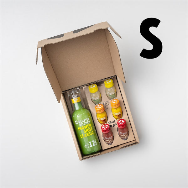 Ginger Shot tasting set S open so you can see the contents: 1x 360 ml Ginger Shot Classic + Shot glass, 2x Ginger Shot Classic 30 ml, 2x Ginger Shot Turmeric 30 ml, 2x Ginger Shot Pomegranate. A large S next to it stands for the size of the tasting set.