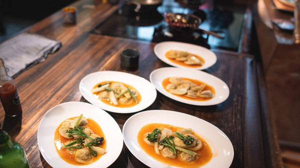 5 plates arranged with eggplant ravioli with tomato broth on a kitchen countertop.