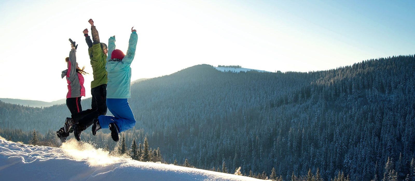 Mit den richtigen Neujahrsvorsätzen ins Jahr starten: 3 Personen auf schneebedeckten Berg springen freudig der Zukunft entgegen.