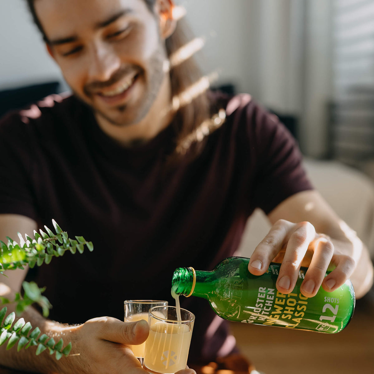Smiling man pouring a drink from a green bottle into a small glass.