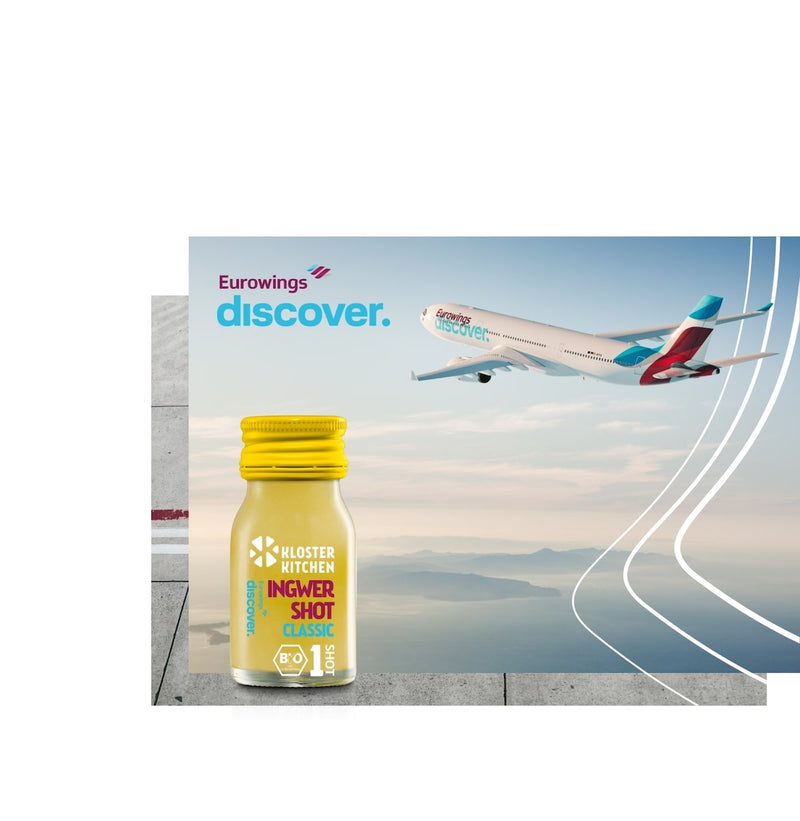 Der Ingwer Shot Classic von Kloster Kitchen + Eurowings Discover. Im Hintergrund sieht man das Logo von Eurowings Discover sowie ein Flugzeug der Airline.