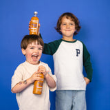 Un ragazzo mette una bottiglia di frutta 12SHOTS da 360 ml sulla testa di un altro ragazzo. Il ragazzo più piccolo in primo piano, che ha la bottiglia sulla testa, ha in mano un'altra bottiglia di shot di frutta 12SHOTS.