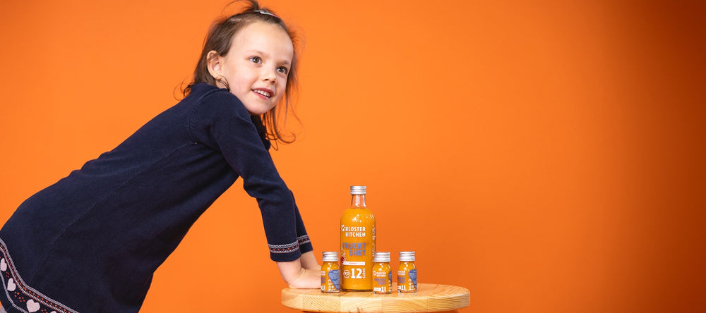Girl leaning on a stool with fruit shots in the large 360 ml bottle and three fruit shots in 30 ml bottles next to it. 