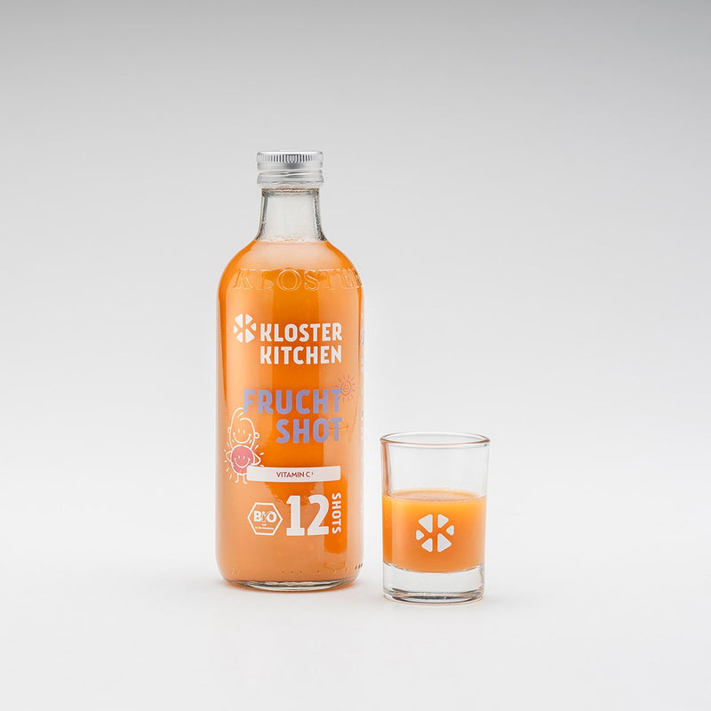 Frucht Shot 12SHOTS in der 360 ml Flasche, daneben ein Shot Glas gefüllt mit einem knallig orangenem Frucht Shot.