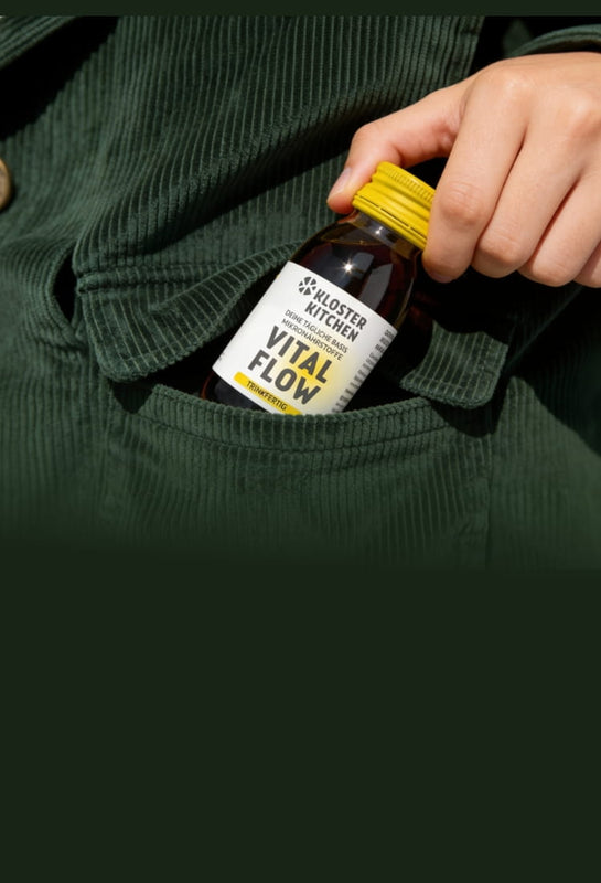 Hand puts a small bottle with a yellow cap and the words "Kloster Kitchen Flow" on it into the pocket of a dark green corduroy top.