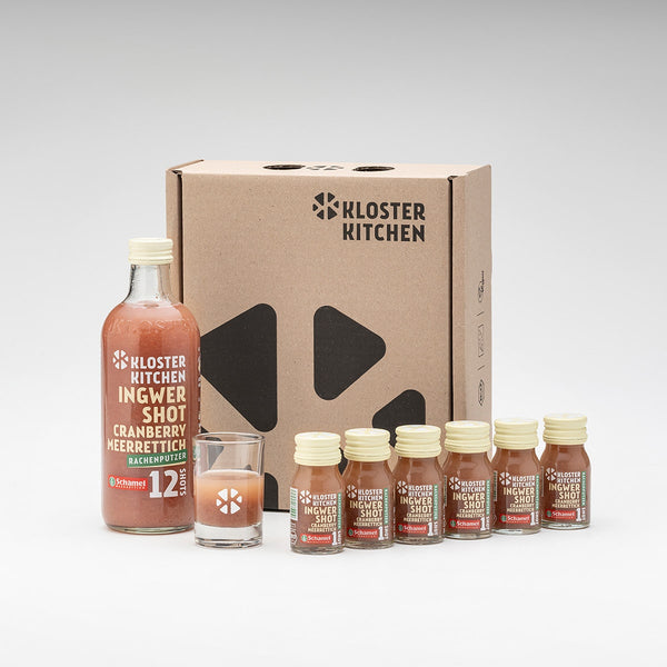 The contents of the Ginger Shot Cranberry Horseradish Box set up in front of the box with 1x 12SHOTS with 360 ml and a shot glass plus 6x Ginger Shot Cranberry Horseradish 30 ml 