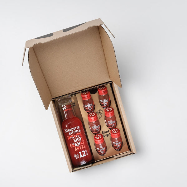 The Ginger Shot Mother's Day open gift box. It contains 6 x 30 ml bottles of Ginger Shot Pomegranate with a limited edition heart design and a 360 ml bottle of Ginger Shot Pomegranate with a limited edition heart design as well as a shot glass.
