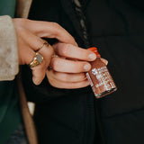 Contents of the Kloster Kitchen gift box Mother's Day: one hand holds a ginger shot pomegranate 30 ml bottle, the hand of a second person meanwhile holds on to the first hand with two fingers.  