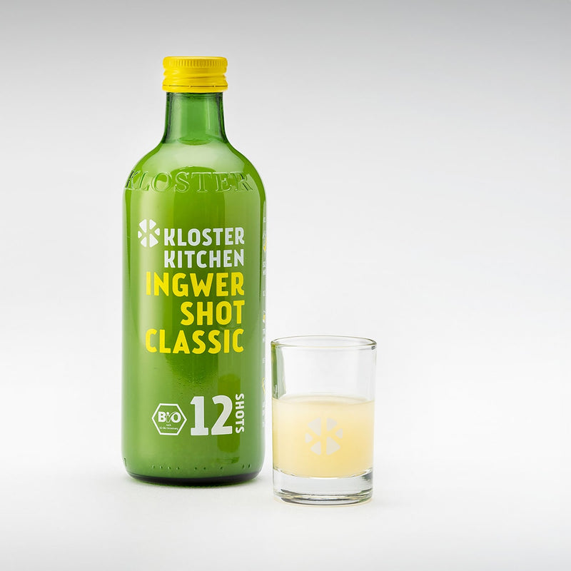 Der Ingwer Shot in der Geschmacksrichtung Classic in der 360 ml Flasche mit einem gefüllten Shot Glas daneben