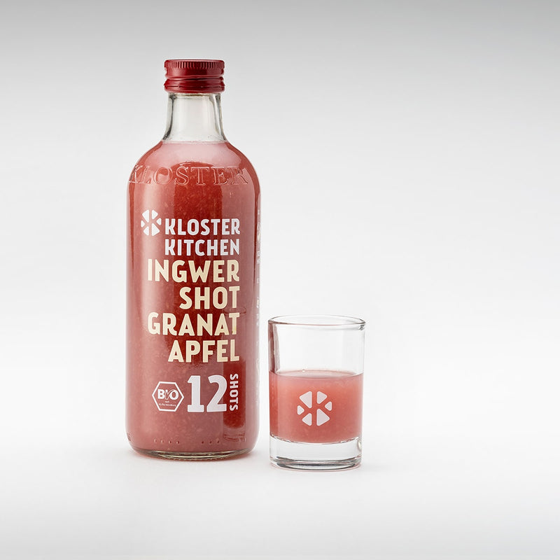 Le shot de gingembre au goût de grenade dans une bouteille de 360 ml avec un verre à shot rempli à côté.