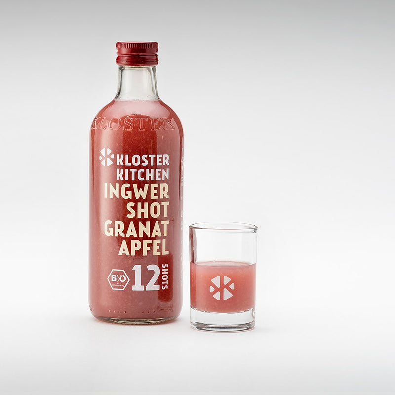 Lo shot di zenzero al gusto di melograno nella bottiglia da 360 ml con accanto un bicchierino riempito.