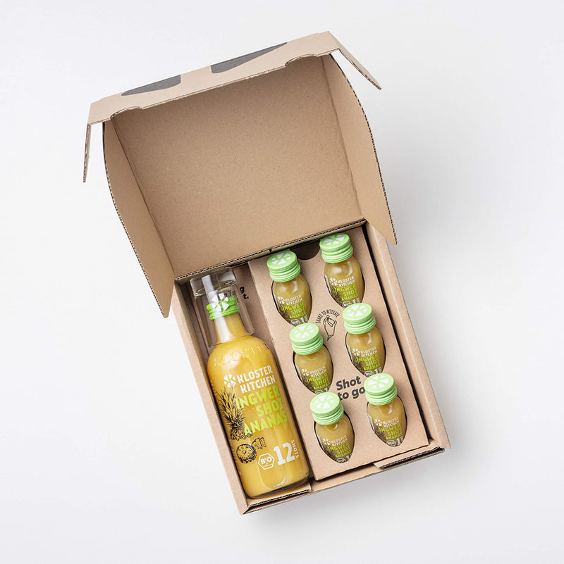 Die Ingwer Shot Ananas Box geöffnet, damit man den Inhalt sieht: 1 360 ml Flasche Ingwer Shot Ananas, 6x 30 ml Ingwer Shot Ananas + 1 Shot Glas.