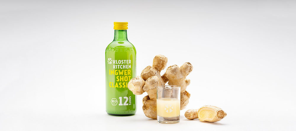 Un Ginger Shot Classic di Kloster Kitchen, accanto un bulbo di zenzero e uno shot versato in un bicchiere da shot.