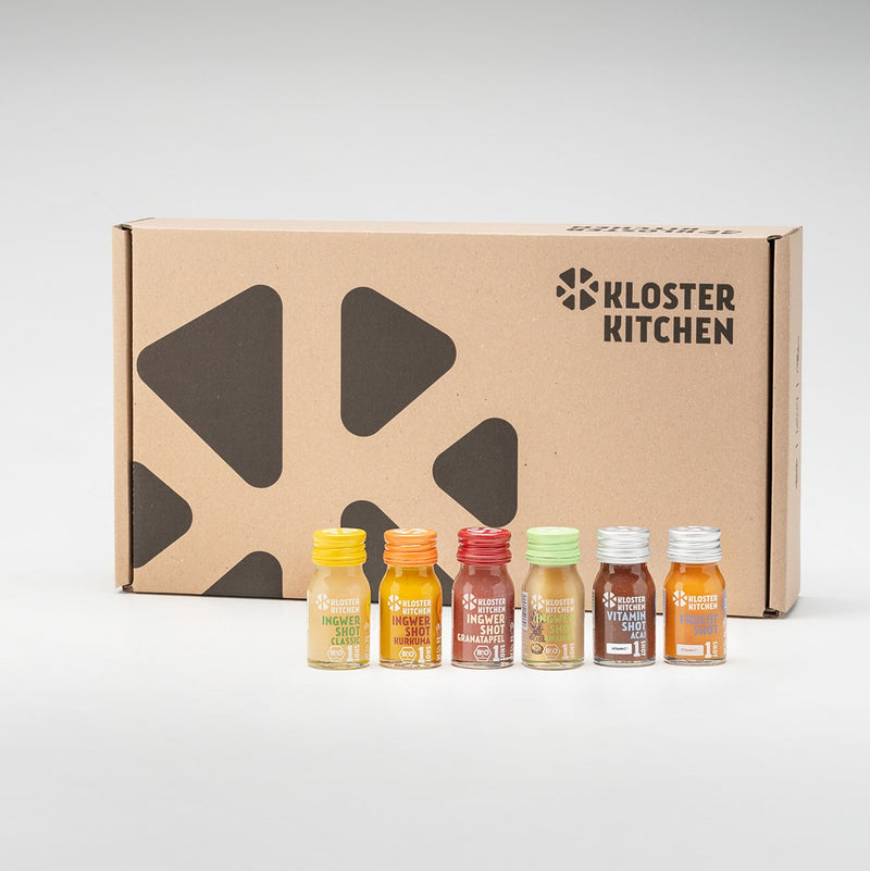 The packaging of the Ginger Shot cure. In front of it are the contents of the cure: a Ginger Shot Classic, a Ginger Shot Turmeric and a Ginger Shot Pomegranate each in a 30 ml bottle