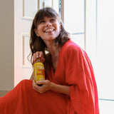 Contents Ginger Shot tasting set M: Ginger Shot Turmeric 360 ml bottle held by a smiling woman in a red dress. 