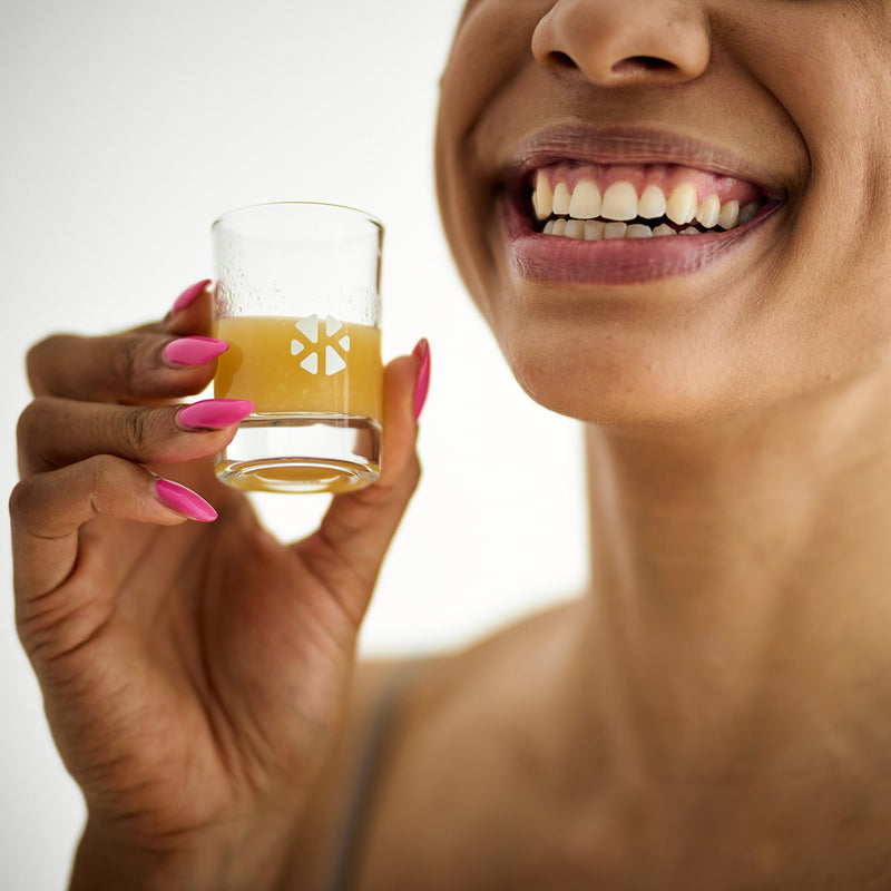 Gläser für Ingwer Shots: Frau hält lächelnd ein Glas für Ingwer Shots hoch.