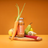 Smoothie apple carrot rhubarb in front of an orange background. The smoothie is on a wooden board and the ingredients are placed next to the bottle: Carrot, apple, rhubarb, pear and a lemon.