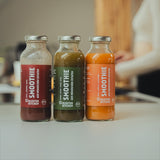 Three Kloster Kitchen smoothies on a kitchen worktop. In the background you can see another person cooking at the stove in a blur.