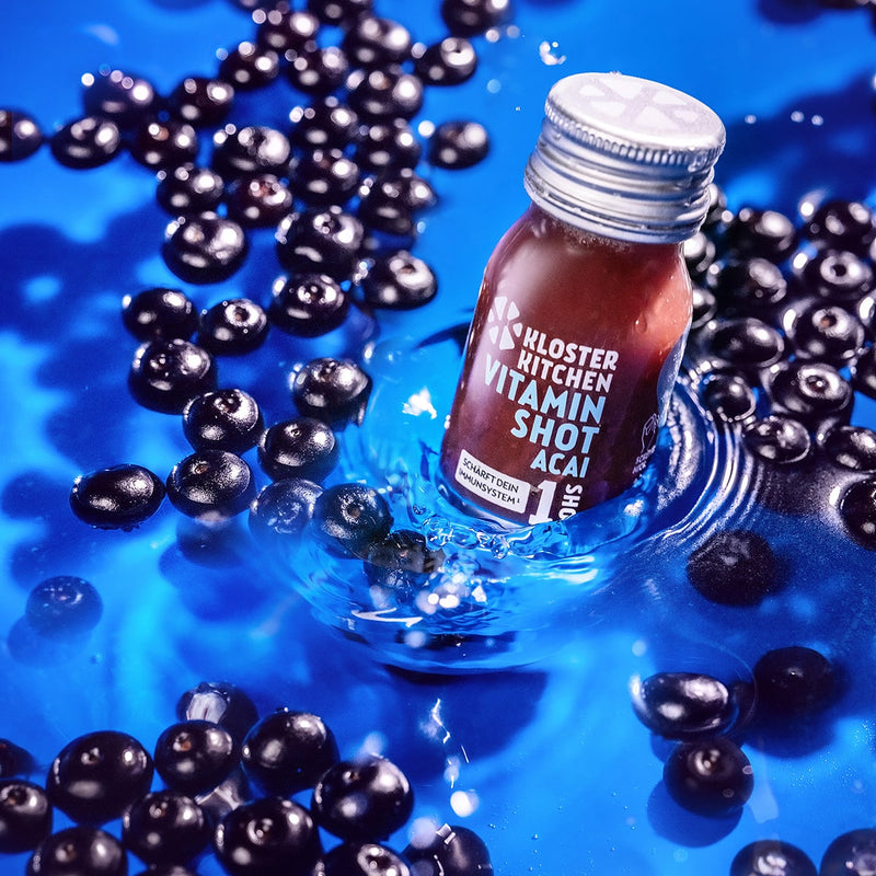 A vitamin shot acai in the water, next to it float some acai berries.