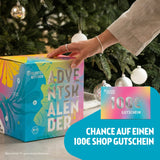 Kloster Kitchen Adventskalender in bunter Kartonbox mit Bio-Siegel, daneben eine Gutscheinkarte mit der Aufschrift 100€ Gutschein, im Hintergrund ein Weihnachtsbaum.
