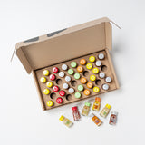 Caja de cartón marrón abierta con 48 tapas redondas de colores dispuestas en una cuadrícula de 8×6; colores como rojo, amarillo, verde, naranja y gris con motivos en forma de estrella sobre un fondo claro.