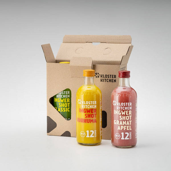 12SHOTS Ingwer Shot Mix Box: 3x Ingwer Shot 360 ml Flaschen. 1x Ingwer Shot Classic noch im Karton, vor dem Karton stehen 1x Ingwer Shot Kurkuma + 1x Ingwer Shot Granatapfel.