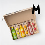 Ingwer Shot Probierset M offen, damit man den Inhalt sieht: 1x 360 ml Ingwer Shot Classic + Shot Glas, 1x 360 ml Ingwer Shot Kurkuma + Shot Glas, 1x 360 ml Ingwer Shot Granatapfel + Shot Glas, 2x Ingwer Shot Classic 30 ml, 2x Ingwer Shot Kurkuma 30 ml, 2x Ingwer Shot Granatapfel. Ein großes M daneben steht für die Größe des Probiersets.