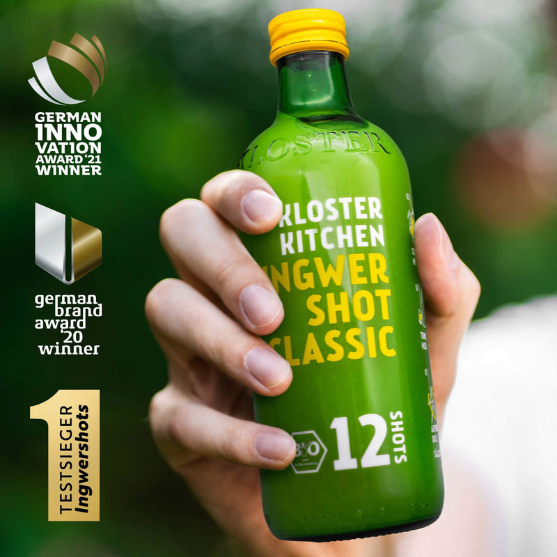 Eine Hand hält 1 von den 3x 12SHOTS 360 ml Ingwer Shot Classic Flaschen hoch, daneben gelistet sind gewonnen Preise. 
